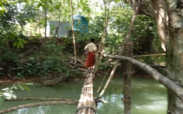 Thumbnail Seorang pria dewasa sedang melewati jembatan bambu hasil swadaya masyarakat yang butuh sentuhan bantuan ( foto : Ach. Suni )